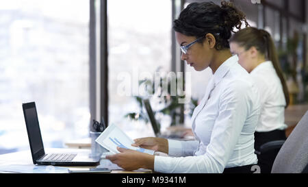 Serious female office manager reading charts, checking data, preparing report Stock Photo
