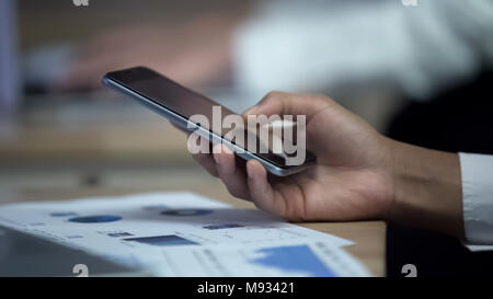 Office worker using smartphone while observing charts, modern technologies Stock Photo