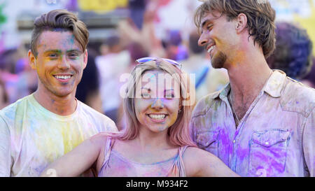 Two handsome men and beautiful woman having fun at color festival, best friends Stock Photo