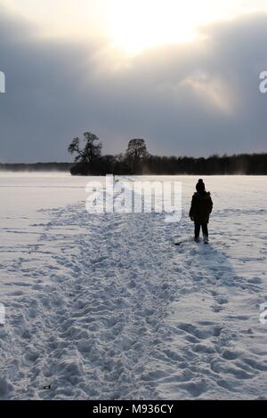 A small figure silhouetted on a snowy path across fields Stock Photo