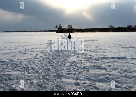 A small figure silhouetted on a snowy path across fields Stock Photo