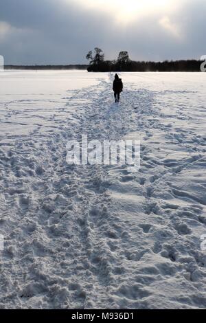 A small figure silhouetted on a snowy path across fields Stock Photo