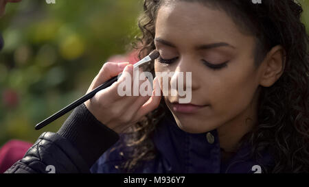 Makeup artist applying eyeshadow on eyes of model or actress, beauty blog Stock Photo