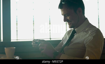 Young happy man watching movie on smartphone in cafe and smiling, gadgets Stock Photo