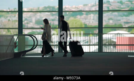 Business trip, man and woman walking to escalator in airport, carrying luggage Stock Photo