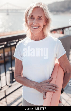 Joyful gray haired woman holding gum rug and smiling. Stock Photo