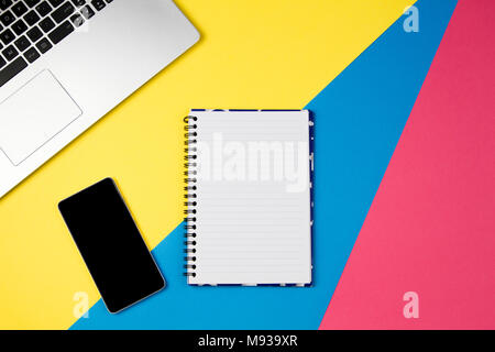 Top view office table desk. Workspace with laptop, smartphone and open spiral notebook page on colorful background. Stock Photo