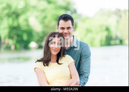 Joyful and spontaneous couple in love, holding hands on a stone pier on a natural lake having fun, kissing, hugging and laughing outdoors. Stock Photo