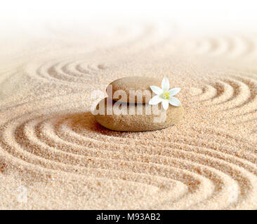 stones and white flower on the sand with circles and waves Stock Photo