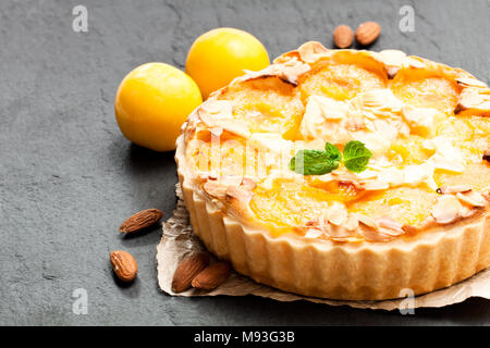Delicious  tart with yellow plum and almonds on black stone background Stock Photo