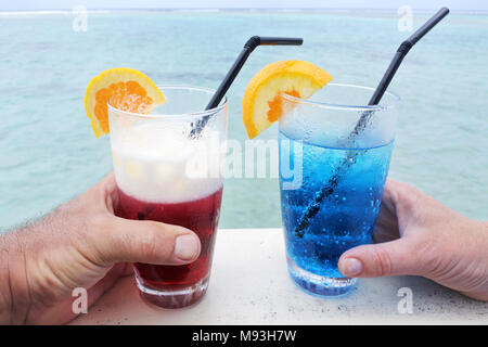 https://l450v.alamy.com/450v/m93h7w/hands-of-a-man-and-woman-holds-a-red-and-blue-cocktail-drinks-with-ice-served-over-a-lagoon-of-a-tropical-island-resorttravel-holiday-vacation-food-a-m93h7w.jpg