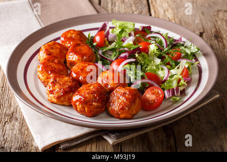 fried glazed meatballs served with salad of lettuce, cherry tomatoes and onions close-up on a plate on a table. horizontal Stock Photo