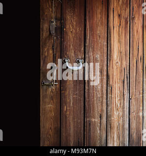 Opened old weathered wooden door with polished metal handle, steel latch and wooden bolt hanging on a string Stock Photo