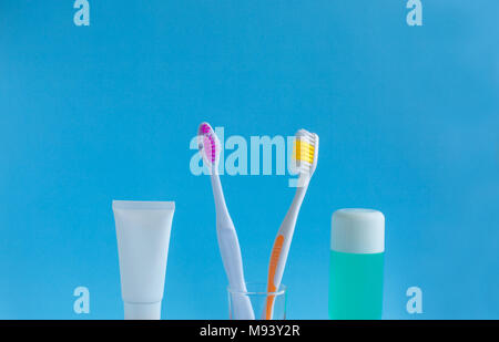 Two toothbrushes in a glass near the toothpaste and rinse against a blue background. The concept of dentistry and health. Free space for copying. Stock Photo