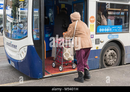 Senior woman boarding a bus with a wheeled shopping trolley in England, UK. Stock Photo