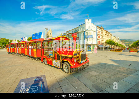 Braga, Portugal - August 12, 2017: red tourist train at the terminus in Praca da Republica crossing Avenida da Liberdade with Tourist Office of Braga on background. Cityscape in a sunny day. Stock Photo