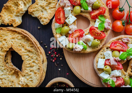 Italian appetizer Friselle. Italian dried bread Friselle on wooden board with tomatoes cherry, olives, tuna, basil and peppercorns. Italian food. Heal Stock Photo