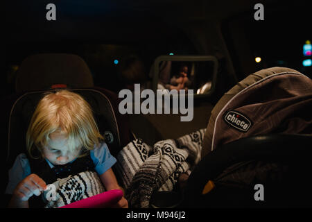 Girl playing on tablet in dimly lit car Stock Photo