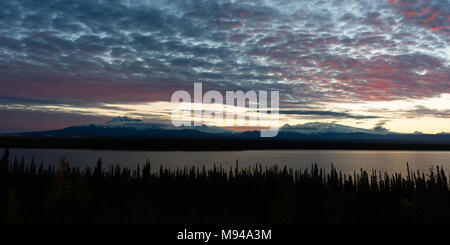 The sun sets reflecting light into the clouds above Willow Lake outside Wrangell St-Elias National Park Stock Photo