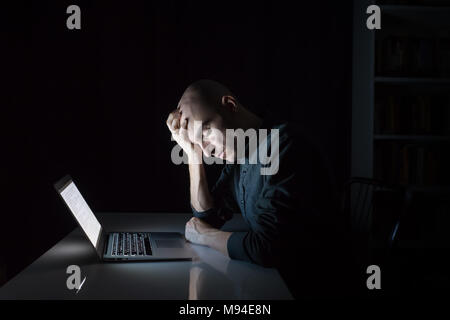 Tired or exhausted man at computer late in the evening with closed eyes. Portrait of young male person working or studying at laptop at night - concep Stock Photo