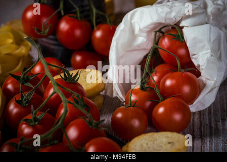 Horizontal photo of several twigs with red cherry tomatoes. Vegetable is placed on wooden vintage board, old worn can or in white paper bag. Tagliatel Stock Photo