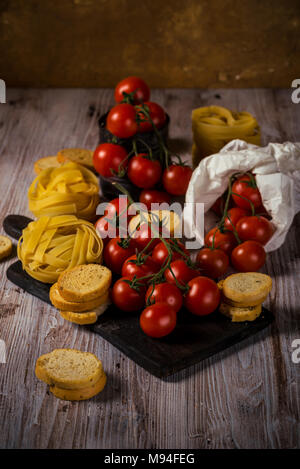 Vertical photo of several twigs with red cherry tomatoes. Vegetable is placed on wooden vintage board, old worn can or in white paper bag. Tagliatelle Stock Photo