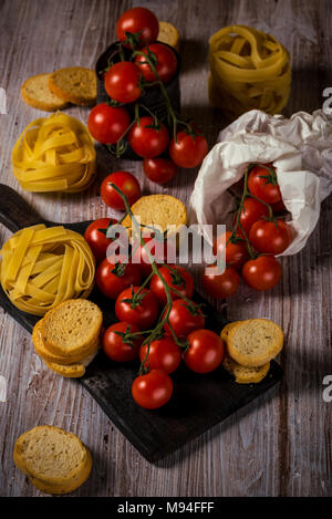 Vertical photo of several twigs with red cherry tomatoes. Vegetable is placed on wooden vintage board, old worn can or in white paper bag. Tagliatelle Stock Photo