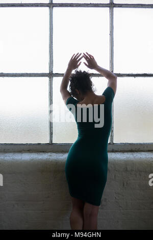 Rear view of a lonely woman standing by the window hands touching the glass Stock Photo