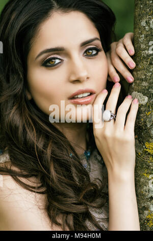 Beautiful young woman wearing makeup leaning against a tree Stock Photo