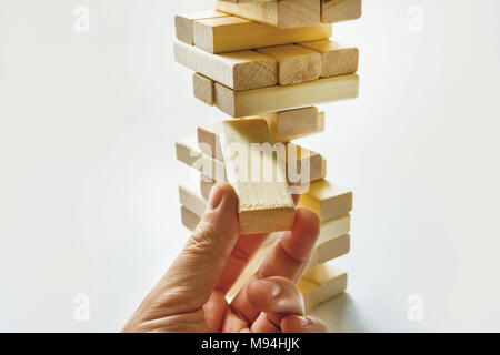 Hand playing with the wood game jenga on white background close-up. Stock Photo