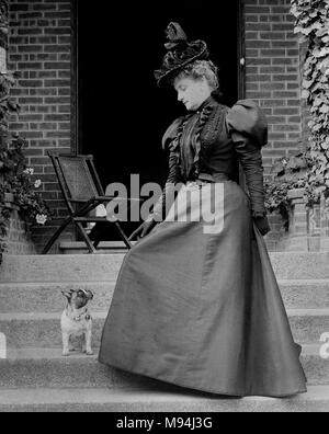 A woman in a large dress has a standoff with a small dog, ca. 1900 Stock Photo