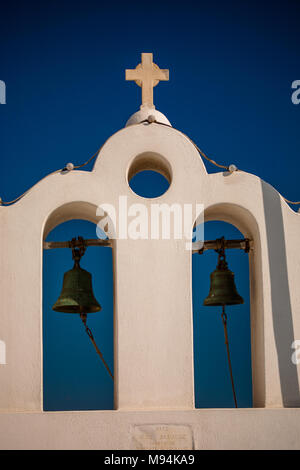 A whitewashed tower of white arches, cross and black bells sits above the Catholic Church in Oia, Santorini, Greece Stock Photo