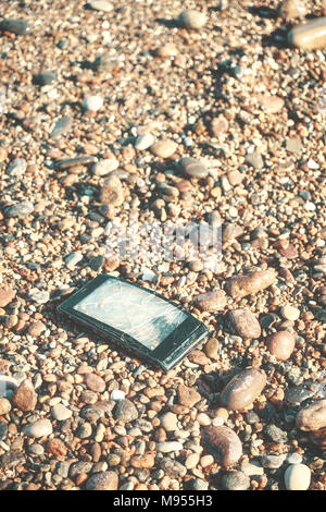 Broken mobile phone with cracked screen on a stony beach, selective focus, color toned picture. Stock Photo