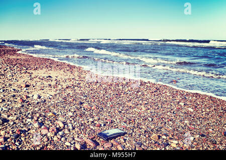 Broken mobile phone with cracked screen on a stony beach, selective focus, color toned picture. Stock Photo