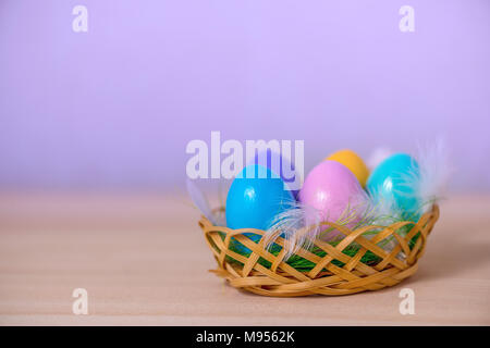 multicolored painted Easter eggs lie in basket with feathers, copy space Stock Photo