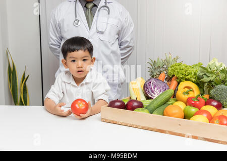 Healthy and nutrition concept. Kid learning about nutrition with doctor to choose eating fresh fruits and vegetables.Young asian boy holding tomato. Stock Photo