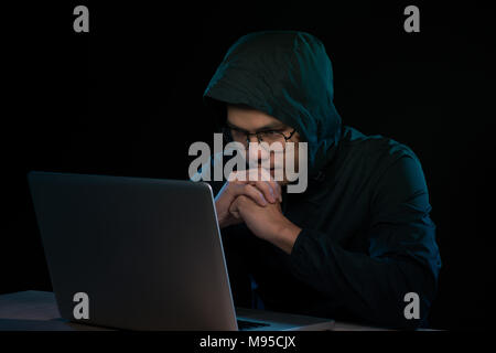 Hacker in a dark hoody sitting in front of a notebook. Computer privacy attack Stock Photo