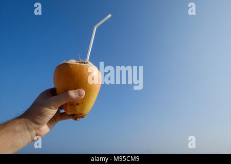 man holding a a coconut on the beach on blue sky background Stock Photo