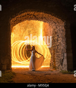 Caucasian white female model with long hair, in a white dress standing and throws gleaming sparks.  Beautiful woman in old building surrounded by lime Stock Photo