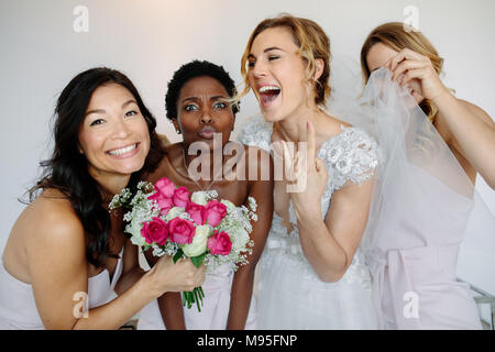 Portrait of cheerful bridesmaids with the bride in the room in the morning. Gorgeous bride in white dress having fun with beautiful bridesmaids in hot Stock Photo