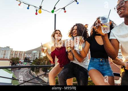 Young people partying on terrace with drinks. Mixed race men and women enjoying drinks on rooftop. Stock Photo
