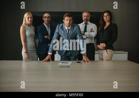 Portrait of confident multi ethnic group of businesspeople looking at camera while standing together at conference table. Corporate professionals in o Stock Photo