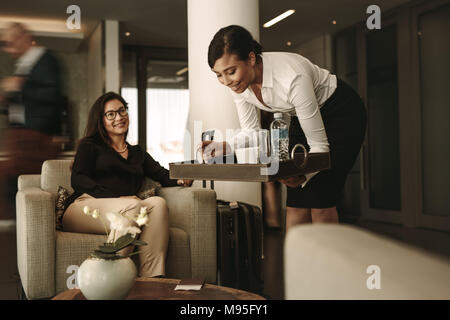Business lounge waitress serving coffee to female passenger at waiting area. Business woman relaxing and waiting for flight at airport departure loung Stock Photo