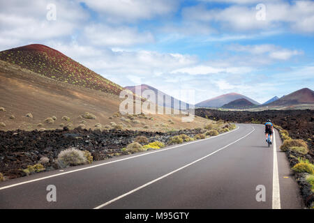 Person riding a bike cycling on an empty road through the El Golfo National Park in Lanzarote Stock Photo