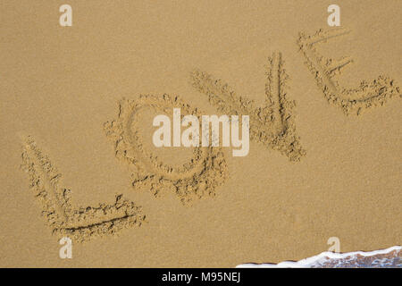 Love and heart symbol handwritten on tropical beach with soft wave on background. Stock Photo