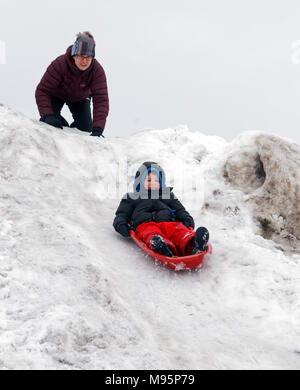 A mum watches anxiously as her son sledges down a very steep icy and wickedly quick slope Stock Photo