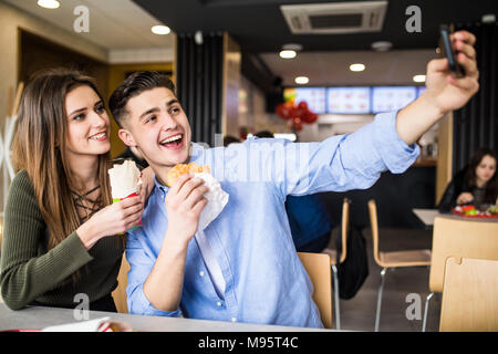 Happy couple eating burger and doner taking selfie together in fast food Stock Photo