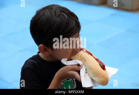 Little HUngry Eurasian Boy Eating a Hot-dog with appetite Stock Photo