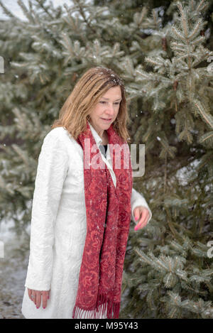 closeup of a woman walking in pine forest in winter with fluffy white snowflakes falling Stock Photo
