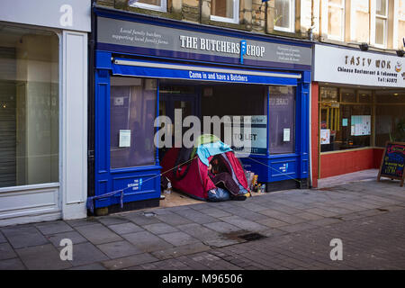 A homeless man and woman living in a small tent outside a disused butchers shop in the centre of Lancaster, Lancashire Stock Photo